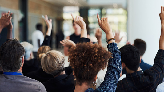 A sitting crowd with their hands in the air to vote.