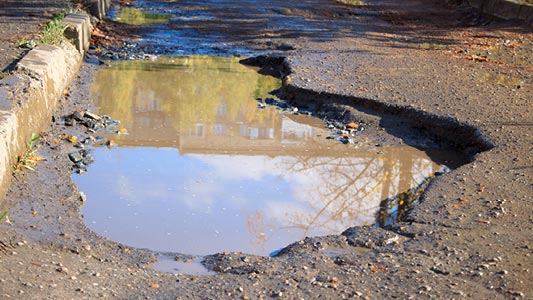 A large pothole filled with water on the side of a street.
