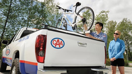 A CAA Manitoba associate repairing a bicycle on top of a CAA truck.