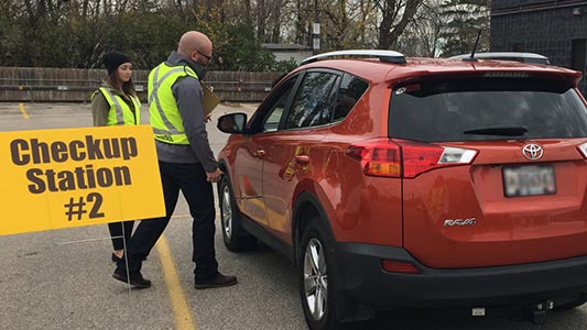A vehicle is greeted by volunteers at a Carfit checkup station.