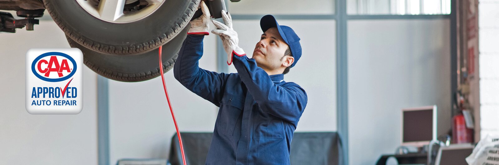 An auto mechanic working underneath a vehicle on a hoist.