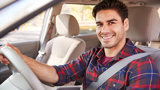 A driver wearing a plaid shirt sitting in his vehicle with his seat belt on.