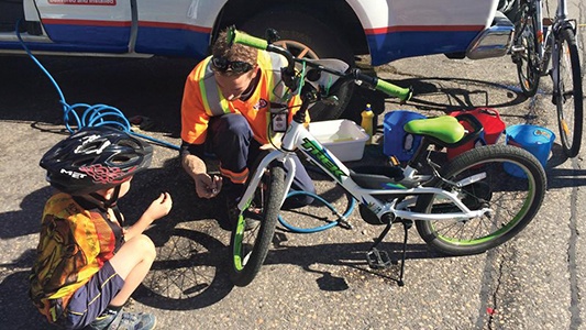 A CAA tow truck driver fixing a bicycle for a cyclist.