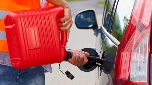 A CAA tow truck driver filling a vehicle's gas tank with gas from a gas can.