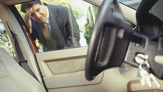 A man looking into his car window and seeing his keys in the ignition.