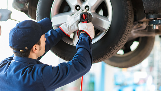 An auto mechanic tightening the bolts on a wheel.