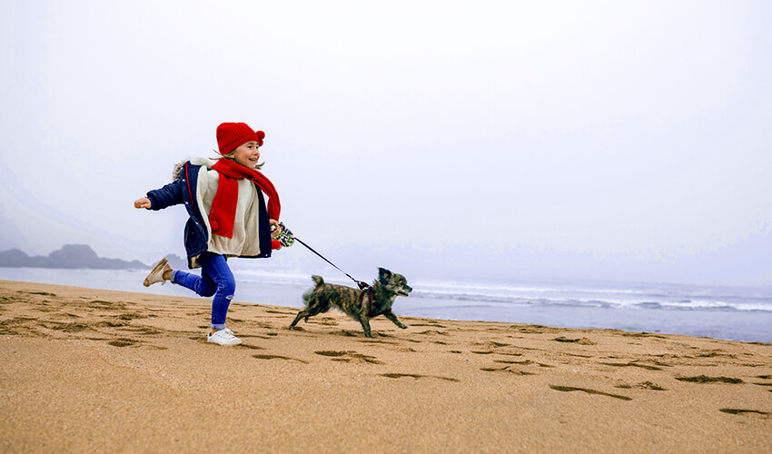 Girl running on a beach with a dog.