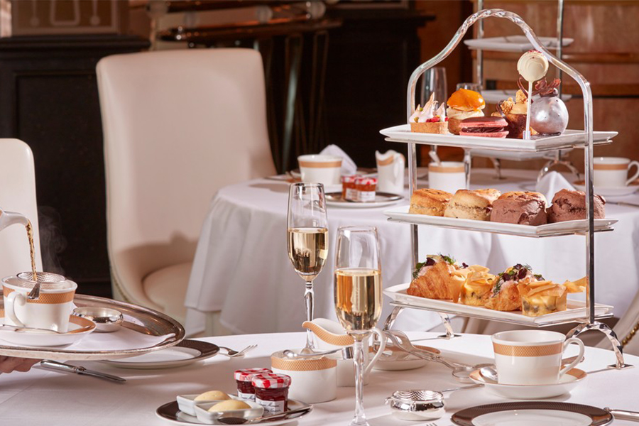 A dining table with a tiered tea tray, tea cups and a champagne flute.