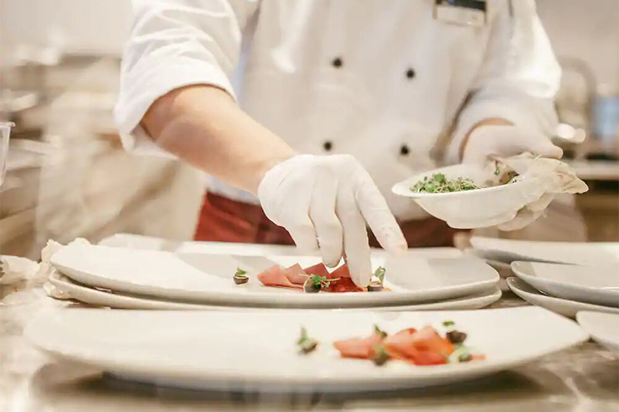 A chef plating a plate with a salmon appitizer.