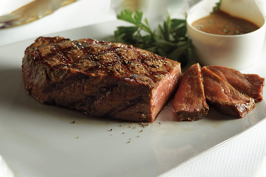 A grilled medium rare steak sliced into strips with a side gravy.