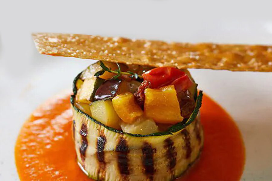 An appitizer of assorted vegetables wrapped with a grilled zucchini slice.