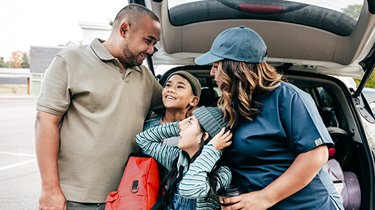 Family of four, smiling and getting ready to go with their car trunk open.