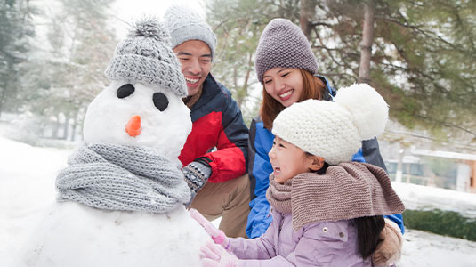 A family of three playing in the snow and building a snowman