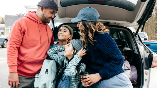 Family of four standing behind an open truck lid of an SUV