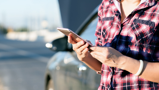 Person holding a phone on the side of the road beside broken down vehicle.