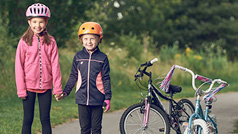 Two kids wearing bicycle helmets standing beside their bicycles.