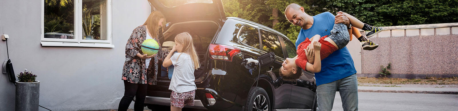 A family of four playing in frond of their car and a house. 