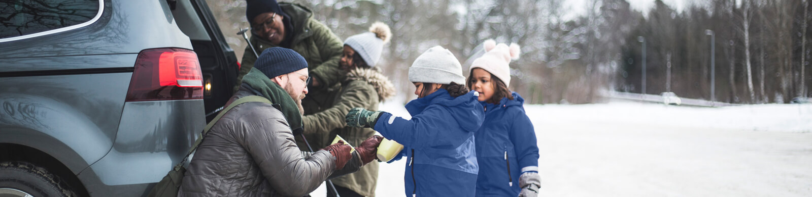 A family with three kids packing a car on a winter road.