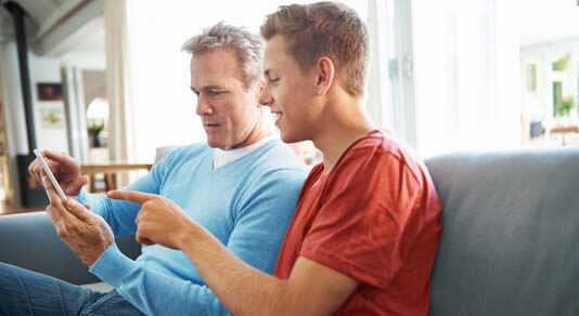 Father and teenage son using phone on the sofa