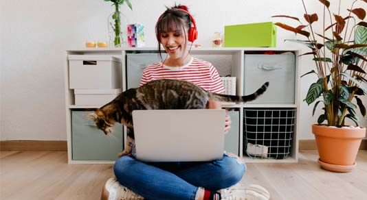 Young woman wearing headphones sitting with laptop and cat at home