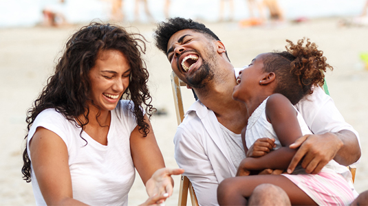 Family of three sitting on the beach laughing