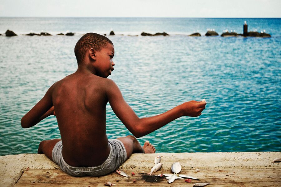 Photo showing young boy with hook and sinker fishing off stone pier with ocean and breakwater in background.