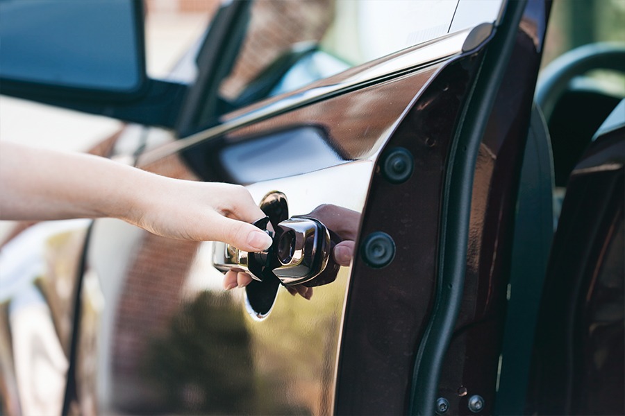 Photo shows hand on car door handle opening door.