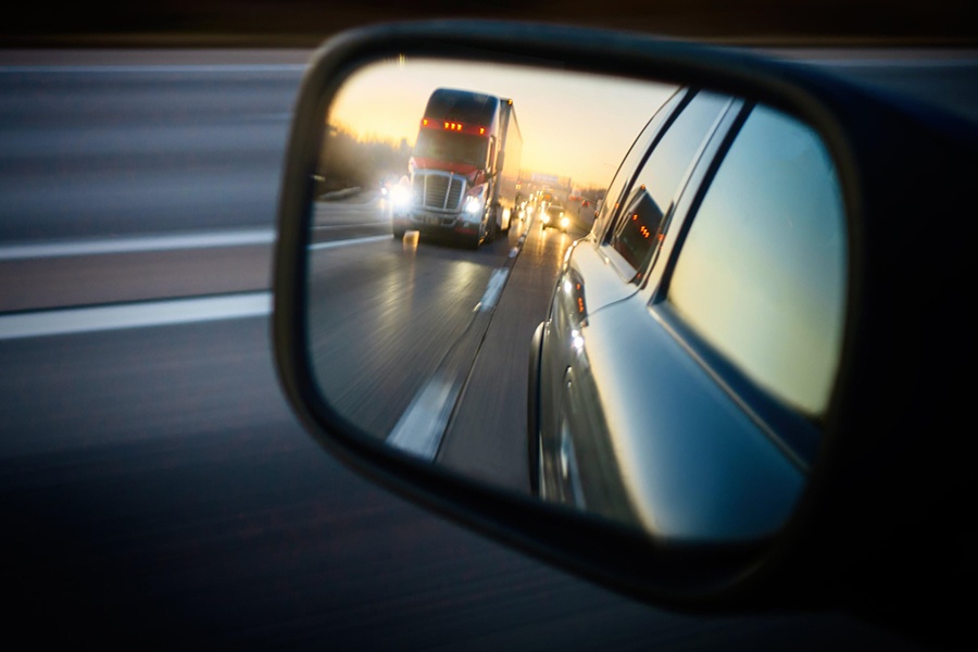Photo of a car side mirror, with an image of a large truck showing inside the mirror.