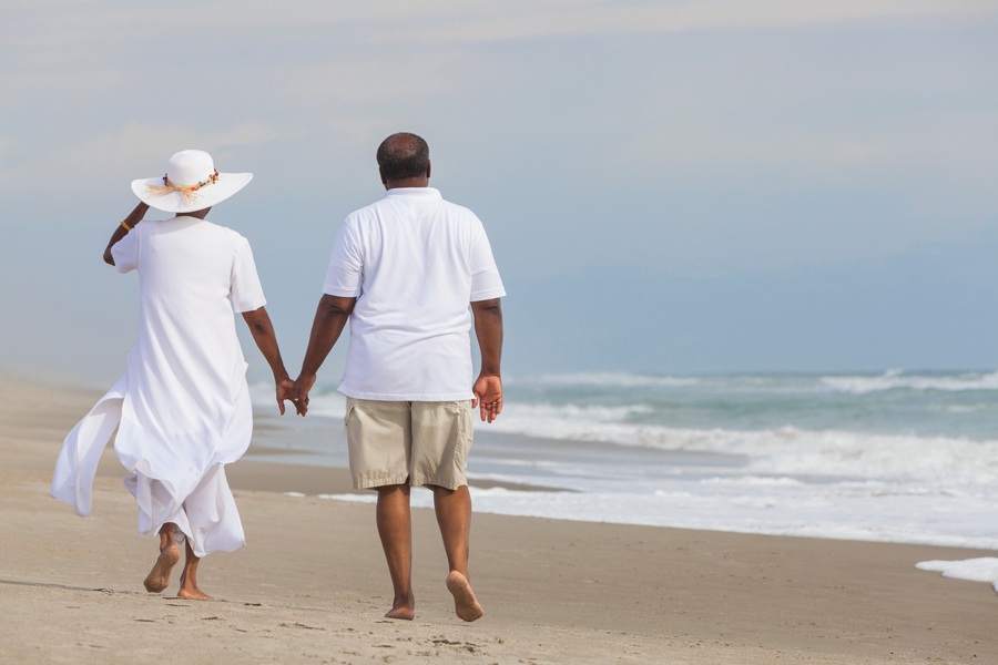 Image of a couple walking hand-in-hand along a sandy beach.