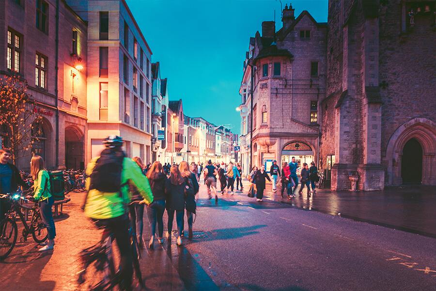 Photo showing pedestrians and cyclists on a street in the light of a setting sun.