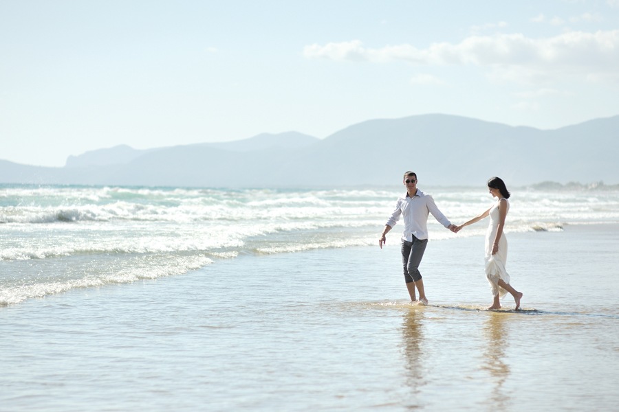Image showing young couple walking hand-in-hand on a beach with ocean surf in the near distance.