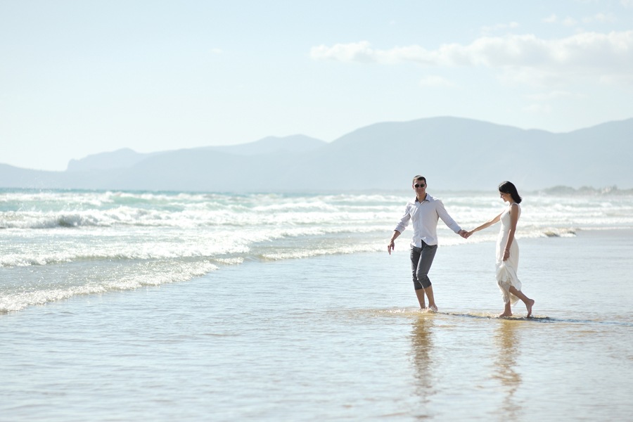 Image showing young couple walking hand-in-hand on a beach with ocean surf in the near distance.