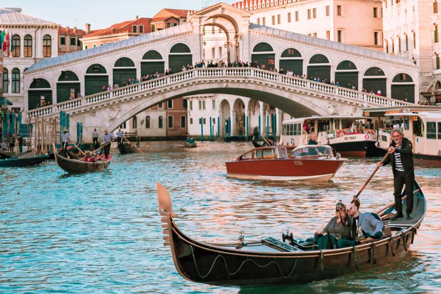 Photo showing bridge over a canal in Venice with a gondola in the foreground.