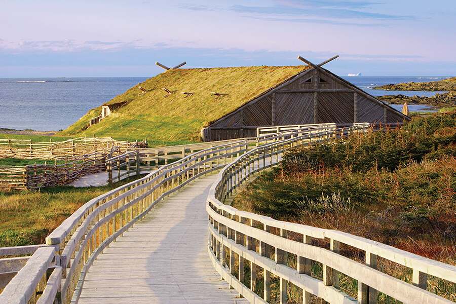 Photo showing a wooden boardwalk leading to a sod covered Viking-style building in the background.