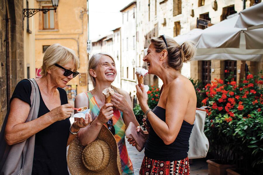 Photo showing three women laughing and eating desserts at a street market.