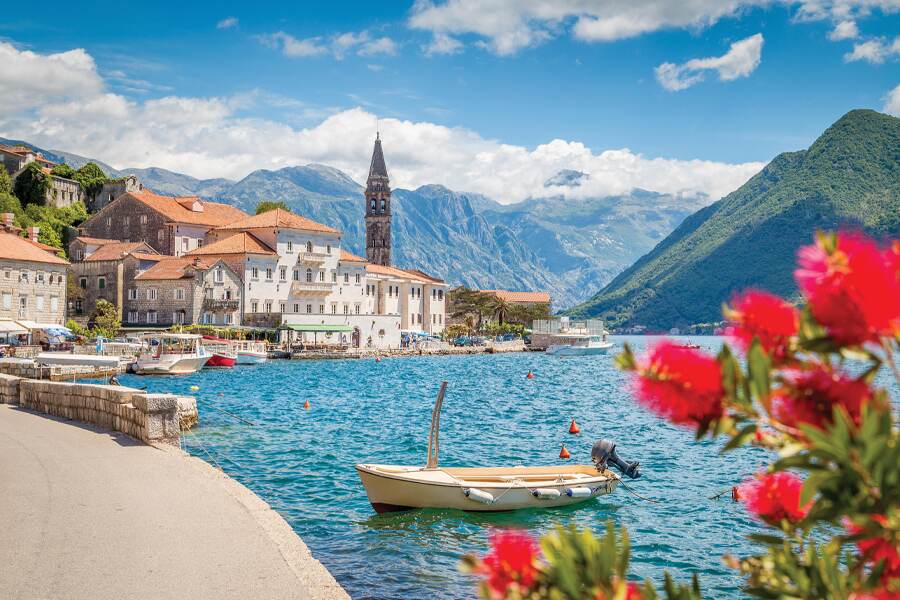 Photo showing rose bouquet and small boat on a lake in the foreground, with a European-style town featured in the background. 