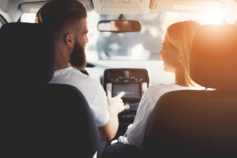 Image taken from back seat showing beadred man driving a vehicle with a woman in the passenger seat.