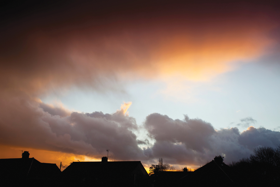 Image showing house roofs in silhouette in the foreground, with a stormy evening sky in the background.