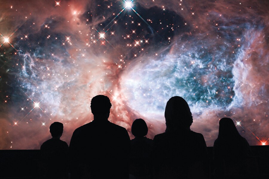 Image of a space galaxy on screen in background, with people silhouetted in the foreground.