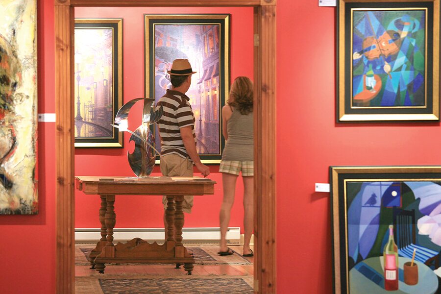 Photo showing man in striped shirt and teenage girl looking at paintings hanging in an art gallery.