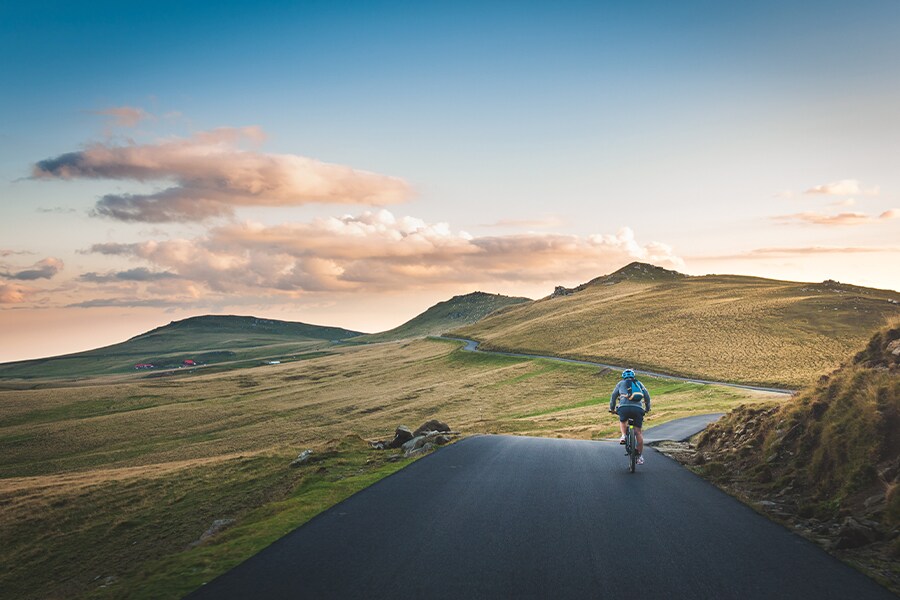 Photo showing lone cyclist pedalling up a gentle slope toward some small hills in the distance.