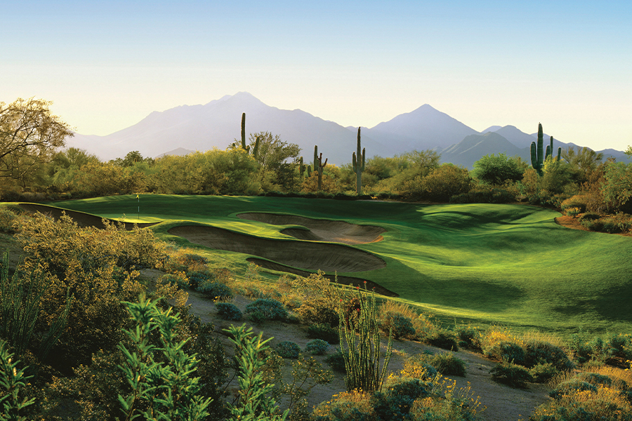 Image showing a lush green golf course surrounded by desert cactus and mountains in the background.