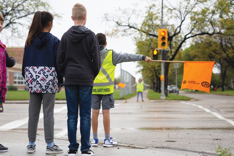 Image showing school patroller with orange flag holding back students waiting to cross the street.