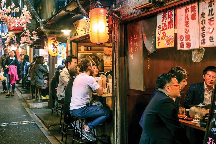 Photo chowing patrons sitting at several street cafes and diners on a Tokyo street at night.