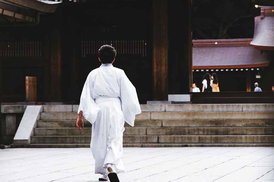 Photo showing a woman wearing white robes approaching the entrance to a Shinto shrine.