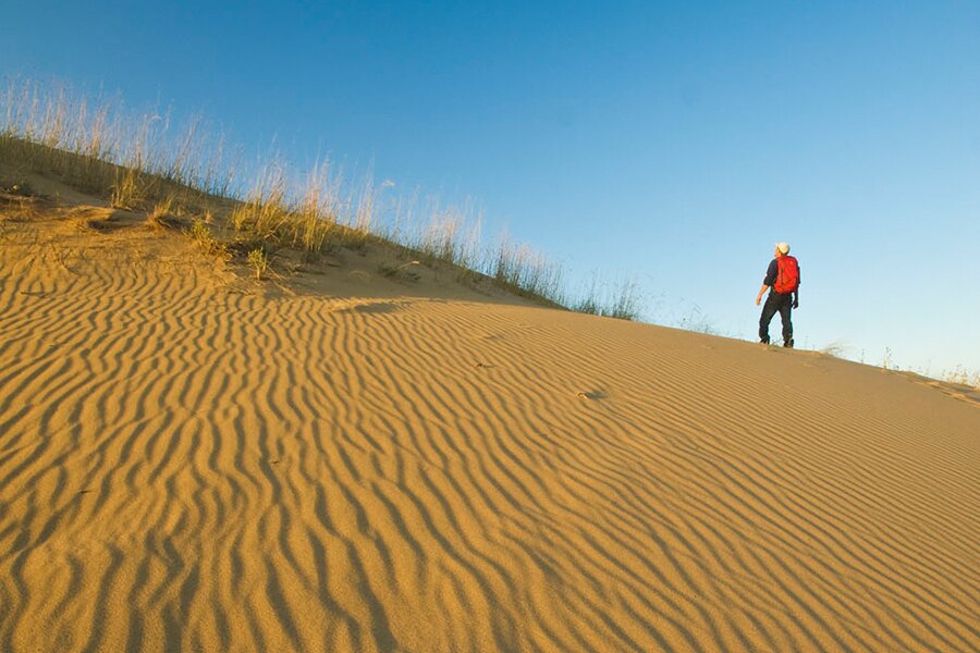 Image showing man hiking up rippled slope of desert-like sand dune.