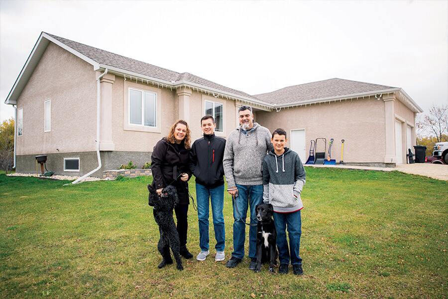 Photo showing family of four with two dogs posing outside their home.