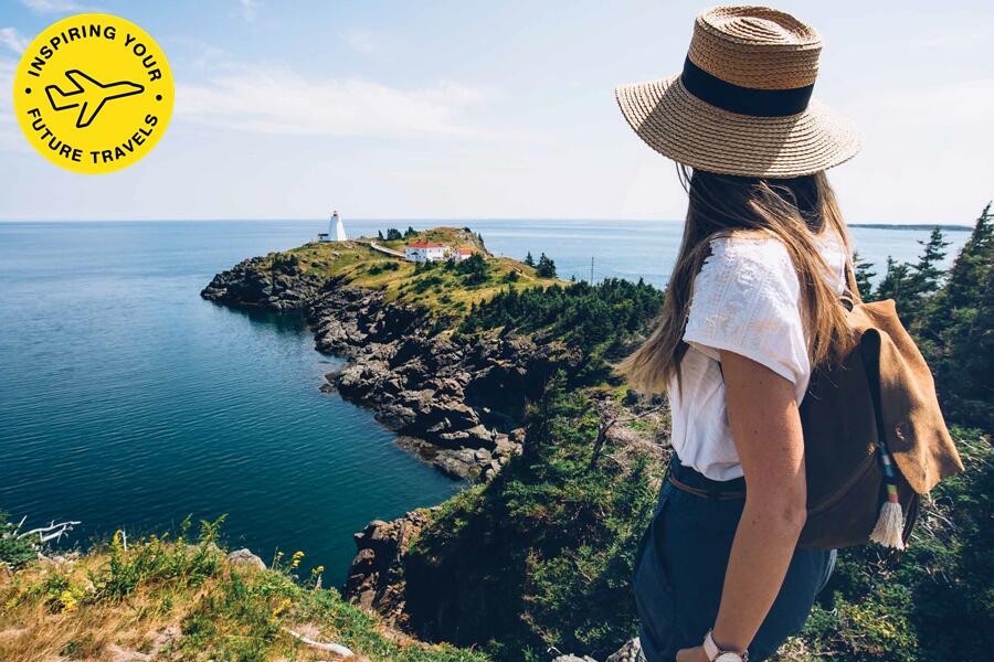 A young woman wearing a hat and backpack overlooking the coast.