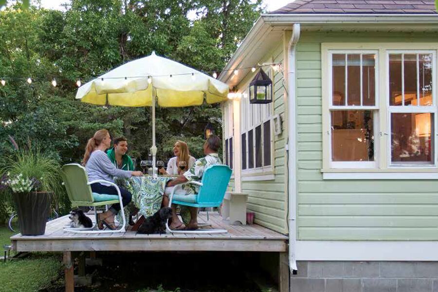 Photo showing two men and two women sitting on a wooden deck attached to a summer cottage, under a yellow shade umbella.