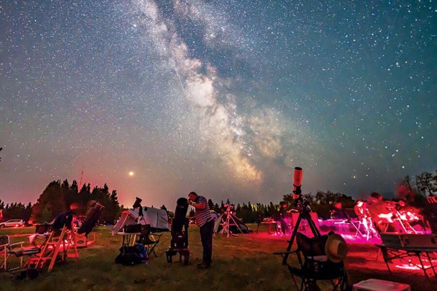 Photo shows people with telescopes in the forground gazing at a starry night sky.